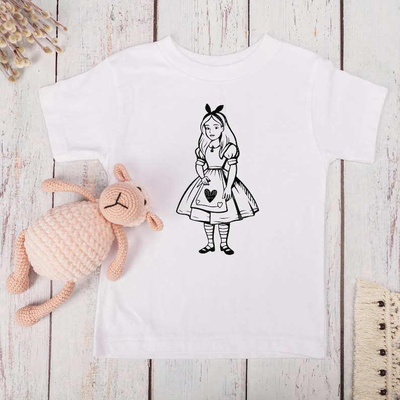 May include: White baby t-shirt with a black and white illustration of Alice in Wonderland holding a playing card with a heart on it.