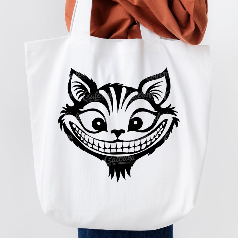 May include: White tote bag with a black and white illustration of the Cheshire Cat from Alice in Wonderland. The cat has a wide grin and large eyes.