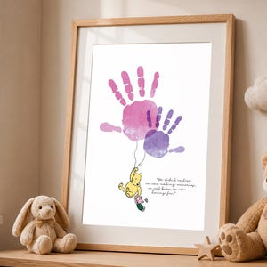 May include: A framed print featuring watercolor handprints in pink and purple hues. A Winnie the Pooh illustration hangs from the handprints, with the quote "We didn't realize we were making memories, we just knew we were having fun!"