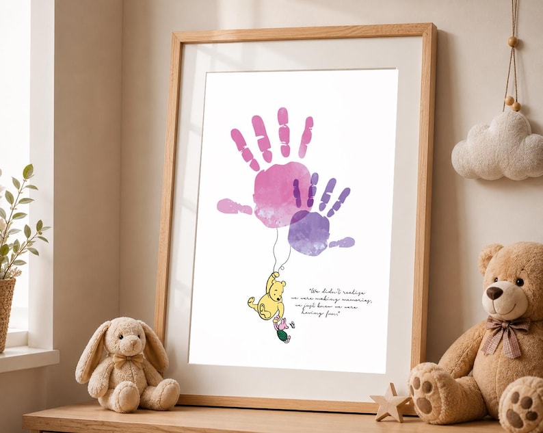 May include: A framed print featuring watercolor handprints in pink and purple hues. A Winnie the Pooh illustration hangs from the handprints, with the quote "We didn't realize we were making memories, we just knew we were having fun!"