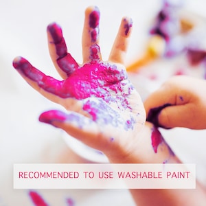 May include: Close-up of a child's hand covered in bright pink and purple washable paint. The text "RECOMMENDED TO USE WASHABLE PAINT" is displayed in a white rectangle at the bottom of the image. The image suggests a fun, creative activity.