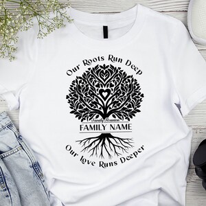 May include: White t-shirt with a black family tree design. The tree has a heart in the center and the text "Our Roots Run Deep" and "Our Love Runs Deeper" around it. The text "Family Reunion FAMILY NAME" is at the base of the tree.