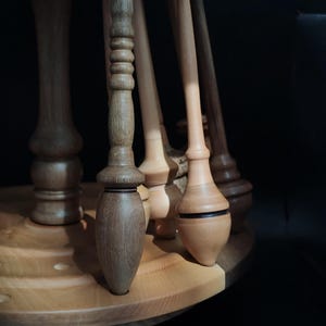 Puede incluir: Primer plano de un soporte decorativo de madera con múltiples patas torneadas. El soporte tiene un acabado marrón claro y una base circular. Las patas varían en forma y diseño, mostrando la artesanía del torneado de madera.