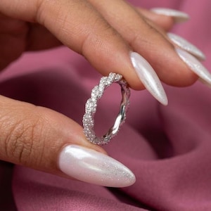 Op de afbeelding: Een zilverkleurige eeuwigheidsring met een gedraaid touwontwerp ingelegd met kleine, heldere, sprankelende steentjes. De ring heeft een doorlopend, ingewikkeld patroon dat rondom de gehele omtrek van de metalen band loopt.