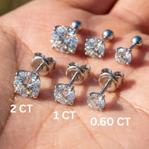 May include: Six diamond stud earrings are shown, with sizes labelled as 2 CT, 1 CT, and 0.60 CT. The earrings have silver posts and feature round, brilliant-cut diamonds. The image displays the earrings in different sizes.