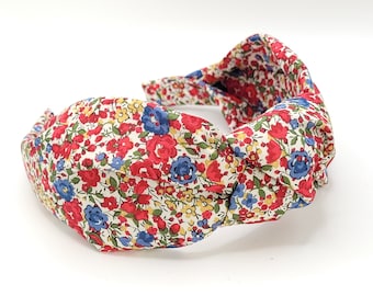 May include: A knotted headband with a floral print featuring red, blue, and yellow flowers on a white background.