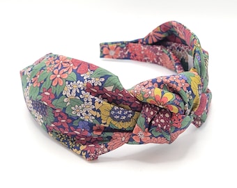 May include: A knotted headband with a floral print in shades of pink, red, yellow, blue, and green on a dark blue background.