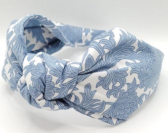 May include: A blue and white floral patterned knotted headband. The headband is made of fabric and has a twisted knot design.