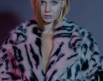 May include: A woman wearing a pink and black faux fur coat with a long, thin silver earring. The coat has a leopard print pattern.