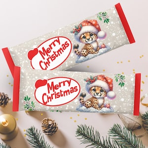 Pode incluir: Duas barras de chocolate festivas com tema natalino com borda vermelha e fundo branco. Cada barra apresenta um guepardo de desenho animado usando um chapéu de Papai Noel e o texto "Merry Christmas" em um design de coração vermelho.