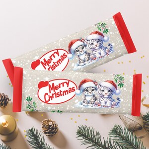 May include: Two white chocolate bars with red and white wrappers. The wrappers feature a festive Christmas design with the words "Merry Christmas" and illustrations of two snow leopards wearing Santa hats.