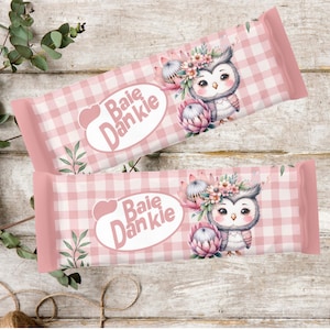 May include: Two pink and white checkered candy bar wrappers with an owl illustration. The owl has a floral crown and is next to a pink flower. The wrappers have the text "Baie Dankie" in a white oval.