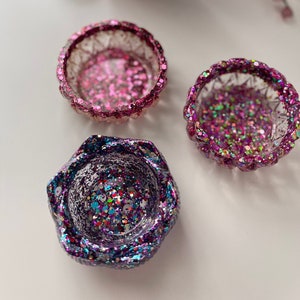 May include: Three small decorative bowls with glitter embedded in the resin. The bowls are pink, purple, and green.