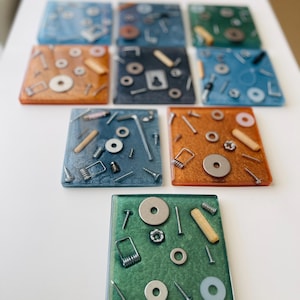 May include: A collection of eight square resin coasters in various colours including blue, green, and orange. Each coaster is embedded with assorted metal hardware, including screws, washers, nuts, springs, and small wooden dowels, creating a textured surface.