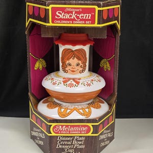 May include: A box of Miramar's Stack-em Children's Dinner Set, featuring a 5-piece melamine set with a dinner plate, cereal bowl, dessert plate, cup, and cup lid. The box shows a stack of the plates with a girl's face on the top plate.