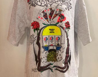 May include: Gray t-shirt with a graphic print of a slot machine with playing cards, roses, and the text "Deadley Yet Skate". The slot machine has the text "Grateful Dead" on it.