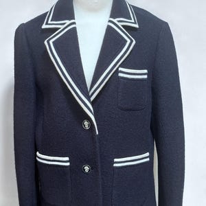 May include: A navy blue blazer with white piping around the collar, pockets, and cuffs. The blazer has two button closures and two flap pockets.