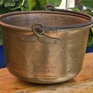May include: A large copper pot with two iron handles. The pot has a hammered finish and is sitting on a wooden surface.