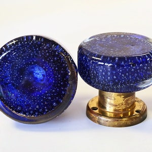 May include: Two blue glass door knobs with brass bases. The glass is textured with small air bubbles.