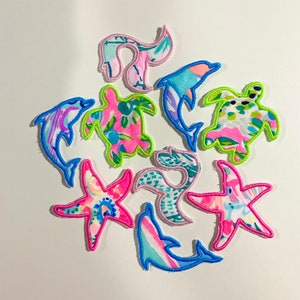 May include: A set of nine colorful iron-on patches featuring sea life designs. The patches include a starfish, a sea turtle, a dolphin, and a wave. The patches are perfect for adding a touch of whimsy to clothing, bags, or other accessories.