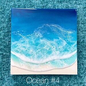 May include: Square artwork depicting an ocean scene. The image features a gradient of blues, from deep navy to light turquoise, representing the water. White foamy waves crash onto a sandy beach. The text "Ocean #4" is at the bottom.