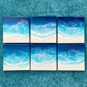 May include: Six square resin art pieces depicting ocean waves. The artwork features shades of blue and white, with a foamy wave effect over a white sandy beach. Each piece is a square, creating a cohesive set.