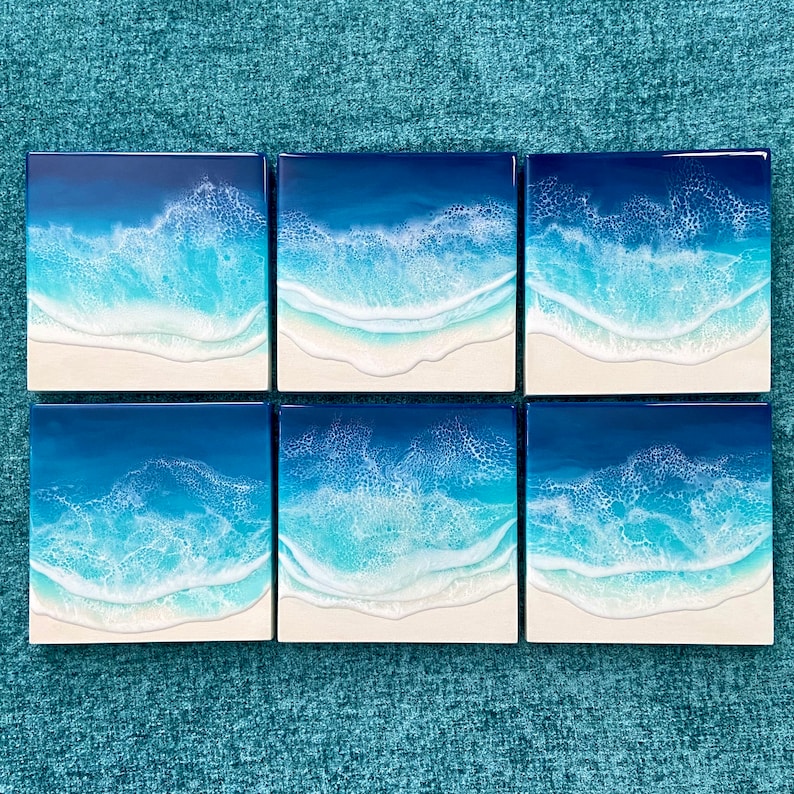 May include: Six square resin art pieces depicting ocean waves. The artwork features shades of blue and white, with a foamy wave effect over a white sandy beach. Each piece is a square, creating a cohesive set.