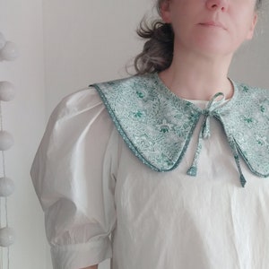 May include: A white blouse with a large, green and white patterned collar. The collar has a tie at the front.