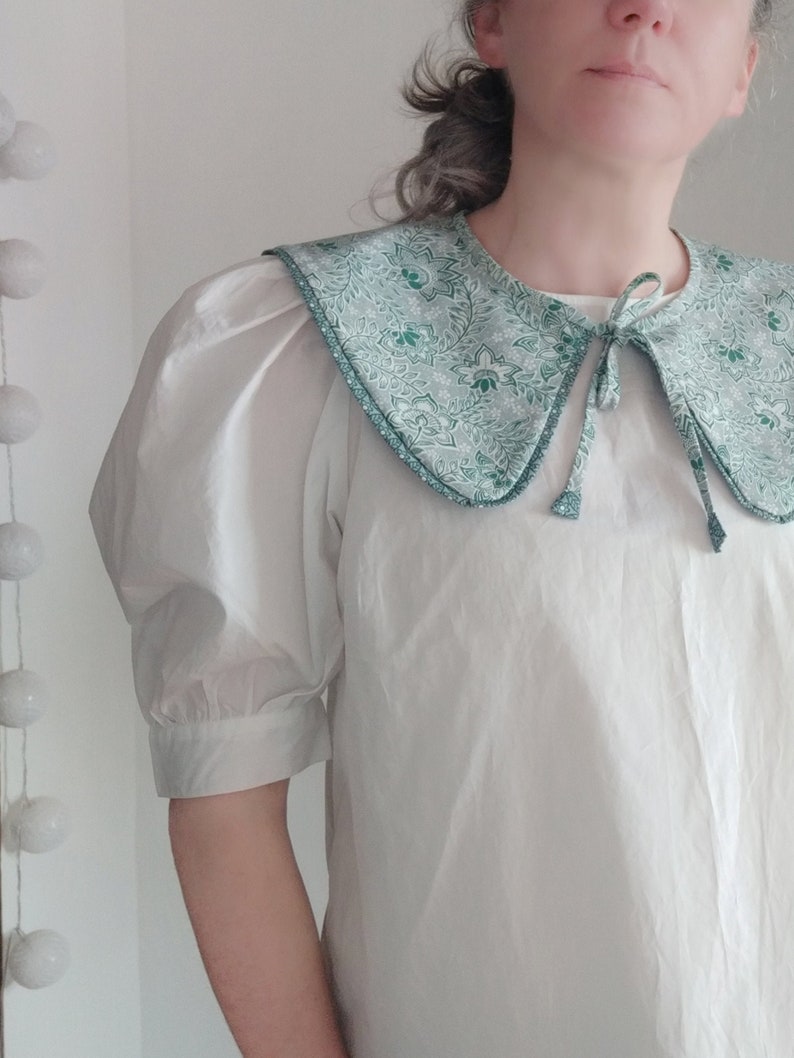 May include: A white blouse with a large, green and white patterned collar. The collar has a tie at the front.