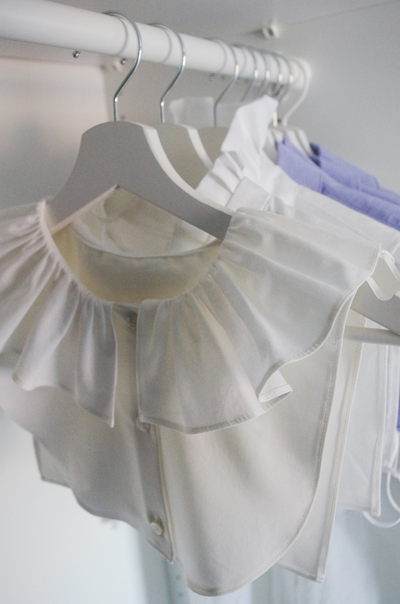 May include: A white ruffled collar on a white hanger. The collar is made of a soft, lightweight fabric and has a delicate, feminine look.