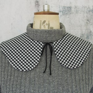 May include: A gray knitted sweater with a black and white gingham collar. The collar has a black ribbon tie.