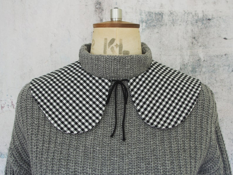 May include: A gray knitted sweater with a black and white gingham collar. The collar has a black ribbon tie.
