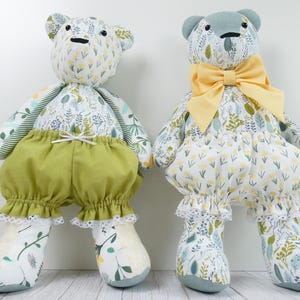 May include: Two stuffed bear toys made from floral patterned fabric featuring yellow and green botanical prints. The left bear wears olive green bloomers with white lace trim. The right bear wears matching floral bloomers and a large yellow bow.