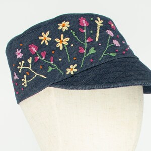 Pode incluir: Um bon&eacute; de brim azul escuro com flores bordadas em rosa, amarelo e verde.