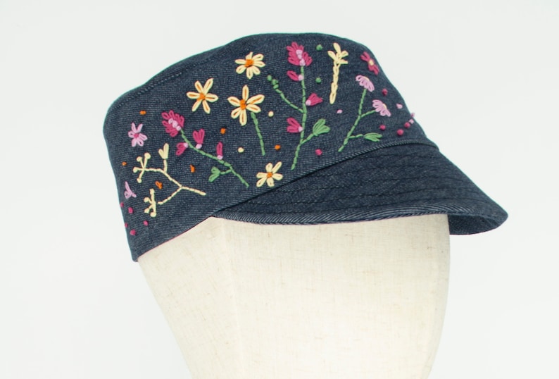 Pode incluir: Um bon&eacute; de brim azul escuro com flores bordadas em rosa, amarelo e verde.