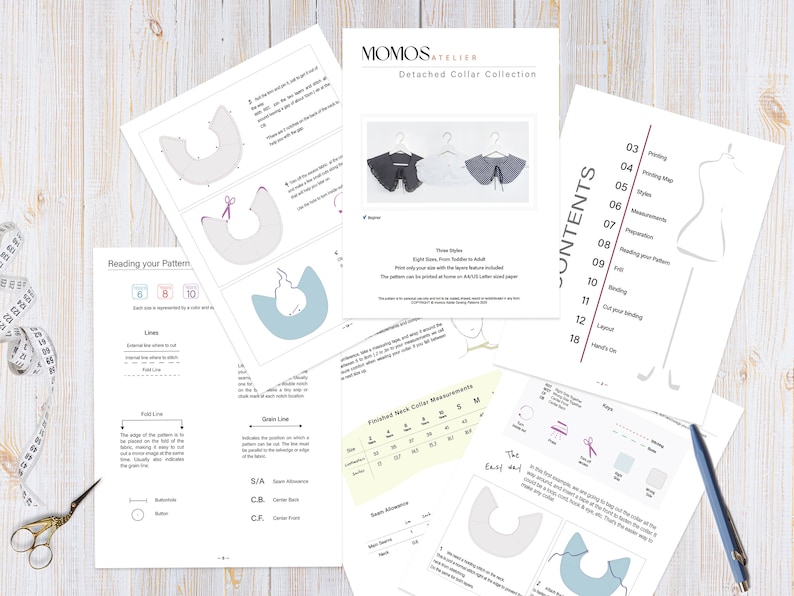 May include: A set of sewing patterns for detached collars in various sizes, from toddler to adult. The patterns are printed on white paper and include instructions for sewing the collars. The patterns are laid out on a wooden table with a measuring tape, scissors, and a pencil.
