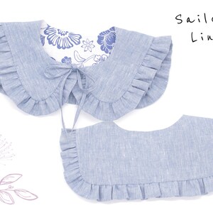May include: Two light blue linen sailor collars with ruffled edges. The top collar has a white floral lining and a tie closure. The text "Sailor Linen" is written in black ink on a white background.