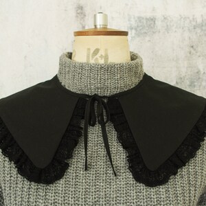 May include: A black fabric collar with a lace trim. The collar is tied at the neck with a black ribbon.
