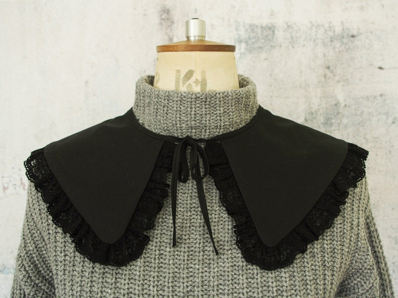 May include: A black fabric collar with a lace trim. The collar is tied at the neck with a black ribbon.