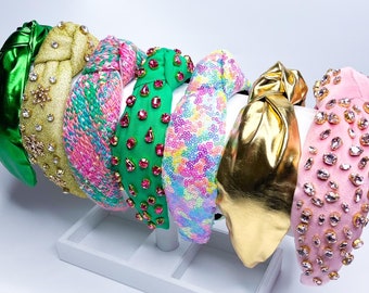 May include: A set of seven colorful headbands with knotted designs. The headbands are decorated with sequins, rhinestones, and glitter.