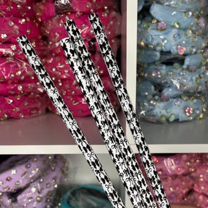 May include: Five black and white striped drinking straws with a bow pattern. The straws are held in a hand.