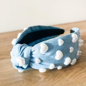 Puede incluir: Una diadema de tela azul claro con un nudo, adornada con adornos blancos en forma de coraz&oacute;n. El accesorio para el cabello tiene un interior oscuro y est&aacute; dise&ntilde;ado para peinar el cabello. La diadema mide unos 15 cm de largo.