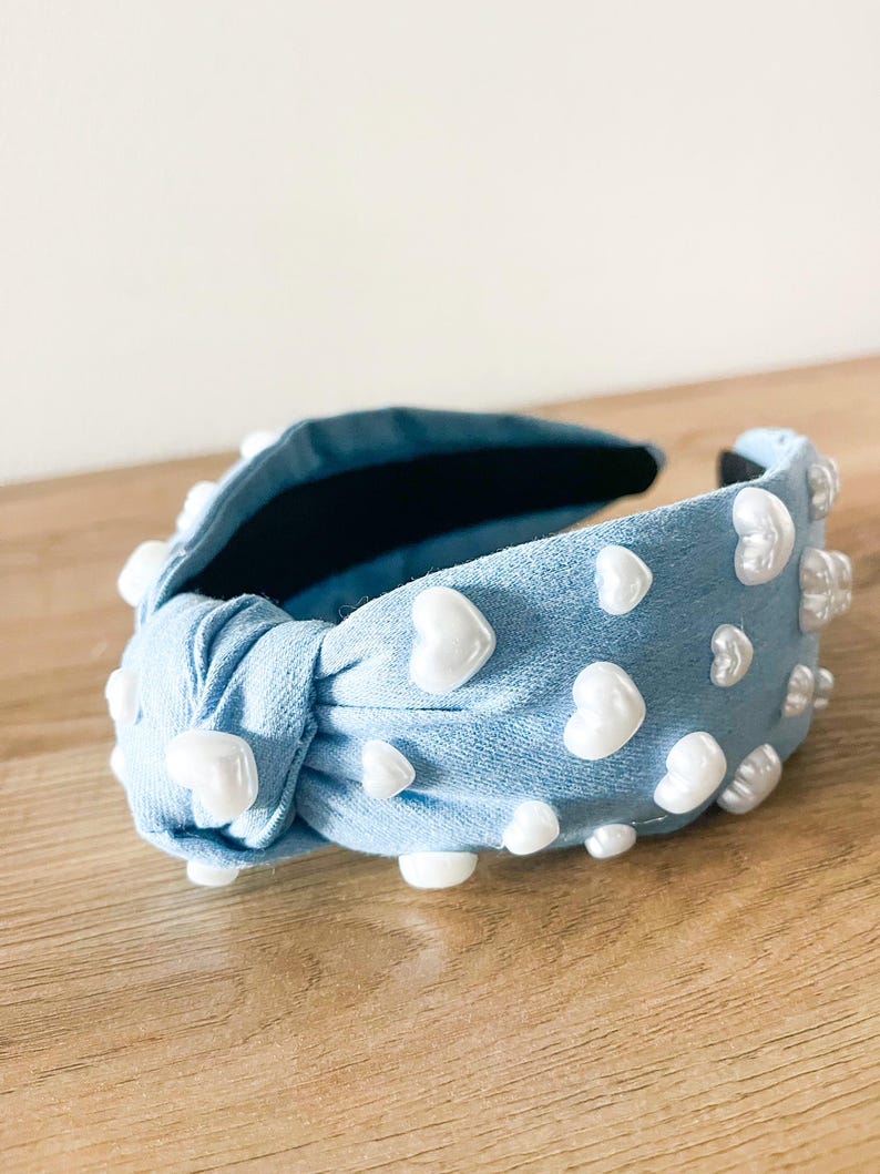 Puede incluir: Una diadema de tela azul claro con un nudo, adornada con adornos blancos en forma de coraz&oacute;n. El accesorio para el cabello tiene un interior oscuro y est&aacute; dise&ntilde;ado para peinar el cabello. La diadema mide unos 15 cm de largo.