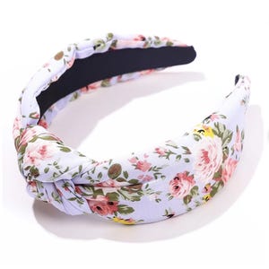 Puede incluir: Una diadema floral con un dise&ntilde;o anudado. La diadema presenta un fondo lila claro con un estampado de flores rosas, amarillas y verdes. El interior es negro.