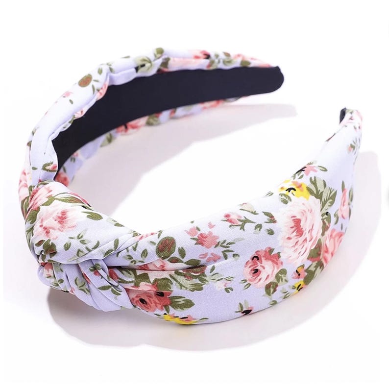 Puede incluir: Una diadema floral con un dise&ntilde;o anudado. La diadema presenta un fondo lila claro con un estampado de flores rosas, amarillas y verdes. El interior es negro.