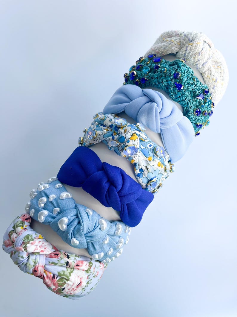 Puede incluir: Una colecci&oacute;n de diademas en varios colores y estilos. Las diademas incluyen una diadema de mezclilla azul claro con detalles de perlas blancas, una diadema con estampado floral y una diadema azul anudada. Otras diademas tienen detalles de joyas y tejidos.