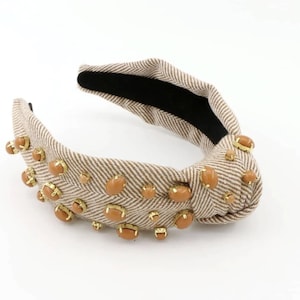 May include: A brown and white patterned headband with a knotted design and brown oval-shaped embellishments.
