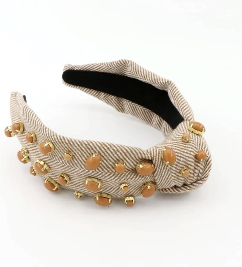May include: A brown and white patterned headband with a knotted design and brown oval-shaped embellishments.