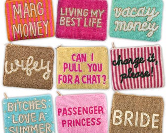 Op de afbeelding: Negen rechthoekige, met kralen bewerkte tasjes met ritssluiting. Elk tasje heeft een unieke tekst: MARG MONEY, LIVING MY BEST LIFE, vacay money, wifey, CAN I PULL YOU FOR A CHAT?, charge it, please!, BITCHES LOVE A SUMMER, PASSENGER PRINCESS en BRIDE.
