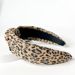 May include: A brown and black leopard print headband with a knotted detail. The headband is made of a soft, stretchy fabric.